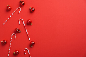 Christmas flat lay composition. Red balls decoration and candy canes on red background. Top view with copy space.