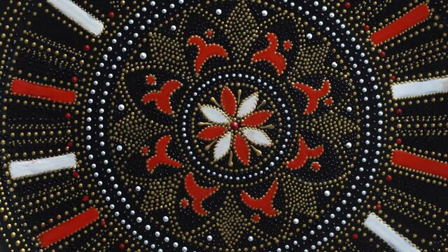 Decorative ceramic plate with red and golden colors, painted plate is rotating on background, close up, top view. Decorative porcelain plate painted with acrylic paints, handwork, dot painting