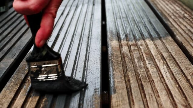 Womens hands Painting faded old Garden Wooden Decking With Grey Paint