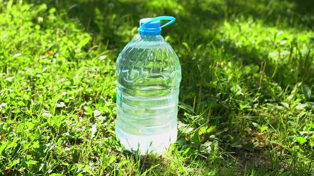 Closeup view video of big transparent plastic bottle size of 5 liters full of fresh clean water standing on grass outdoors in bright sunlight.
