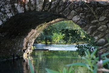 Fototapeta na wymiar The river of the Garden of Ninfa, medieval stone bridge over the lake, relaxing view, Italy
