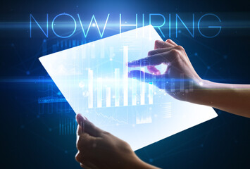 Hand holding futuristic tablet with NOW HIRING inscription above, modern business concept