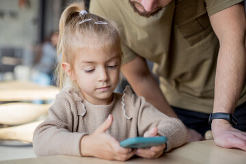 father showing to daughter cool video on smartphone in internet. Parental control, protect child...