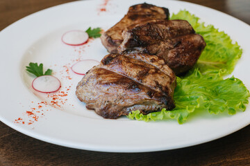 Fried beef meat lies on a green lettuce leaf. Dish on a white plate on a brown table