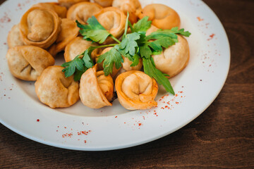 Fried dumplings with green parsley leaves on a white plate. A portion of meat in the dough. Russian...
