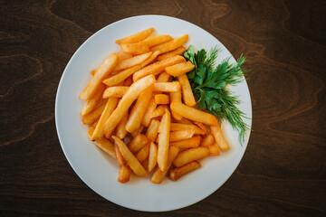 Fried potatoes in oil with herbs. Sliced golden slices with dill. Fast food on a white plate. Dish on a wooden table