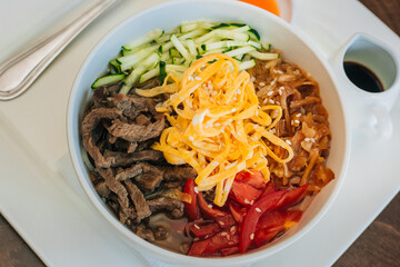 Asian cold soup. Kuksi is a traditional Korean dish. With vegetables and beef in a ceramic white bowl on a dark wooden table, horizontal