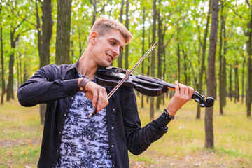 young male play on the violin in the summer park	