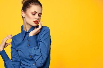 Portrait of a woman in a blue shirt with bright makeup red lips yellow background cropped view