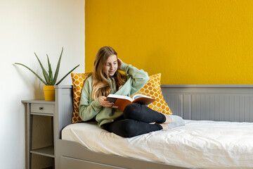 Young blond girl reading book at home
