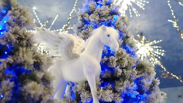 Magic christmas elf horse with white and golden wings among the shining christmas trees, amazing winter holidays decorations performed in the hall. Winter polar symbol of christmas holidays
