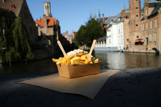 The traditional street food snack, the Belgian Fries with pepper sauce pictured on the wall over the channel in Bruges in Belgium. 