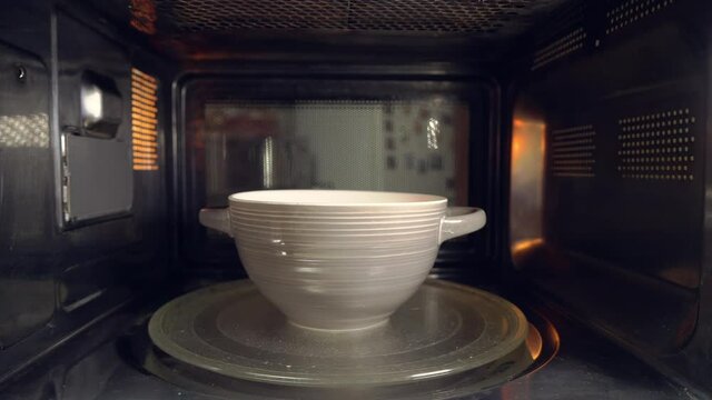 A ceramic bowl with some food is heated in the microwave, spinning , a man's face nervously and discontentedly looks into the microwave through the glass, and takes the plate.