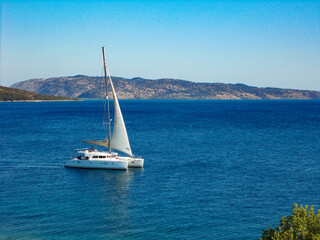 Fototapeta premium White catamaran yacht sailing boat alone on blue sea and cloudless sky