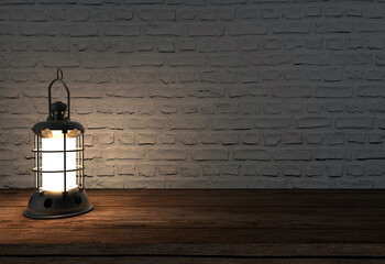 old lamp burning on wooden table in front of stone wall