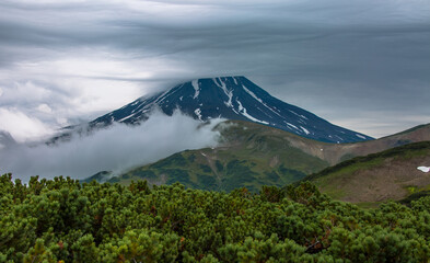 Naklejka na ściany i meble The top of the volcano rests against a cloudy cloudy sky