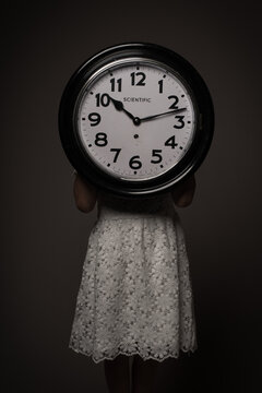Studio portrait of girl in white dress holding large clock in dark rembrandt style