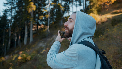 Young traveler with long hair, long bearded hipster man is taking landscape photos with his phone in the forest in the trees. Technology concept