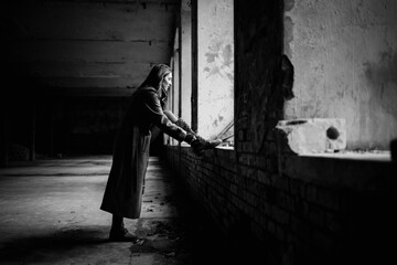 Moody black and white photo of young caucasian woman lacing her boots in abandoned and partly destroyed building with large windows. Daylight. Youth lifestyle and fashion concept.