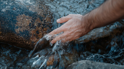 Person hand put in the flowing river or stream and is captivated by the water, close-up slow motion lifestyle nature concept