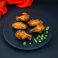Fried chicken drumsticks on the black stone tray with some green onion