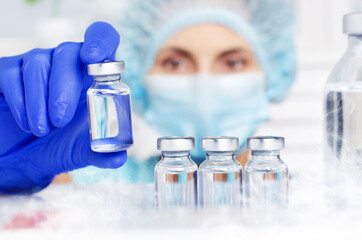 Female nurse in safety mask and gloves takes vial with liquid medicine from refrigerator shelf