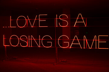 A bright neon LED sign that reads "love is a losing game"