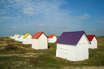 Fototapeta na wymiar The tiny white beach cottages with colorful roofs at a beach by Gouville-sur-Mer in France in Normandy. The attraction for the tourists. 