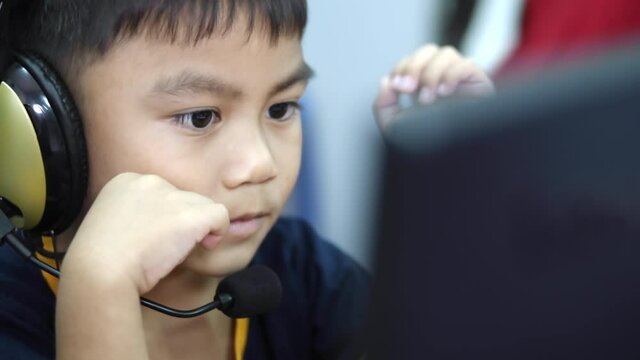 A three-year-old Asian boy is learning from a desktop computer wearing a headset with joy and anxiousness at the kindergarten.