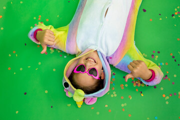 little girls in bright costumes lie on a green isolated background with a streamer in bright unicorn costumes. Space for text. The concept of a holiday, Birthday and sales