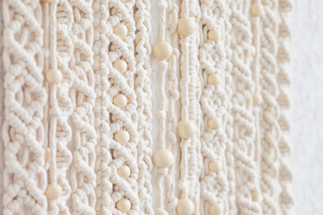 Close-up of hand made macrame texture pattern. Eco friendly modern knitting. Natural decoration concept in the interior. Handmade macrame wall hanging 100% cotton and wooden beads. Soft focus