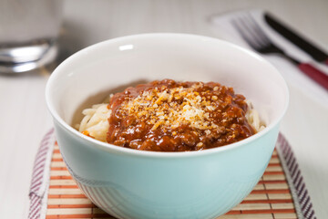 Spaghetti pasta with tomato sauce in white and blue bowl, white wooden background and resting straw plate and cutlery on the side, Brazilian cuisine copy space, top view. Food concept. Pasta concept.