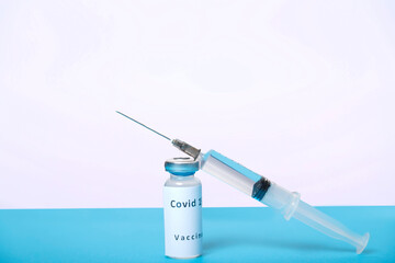 A syringe and a vial with a virus vaccine are on a blue table, top view.