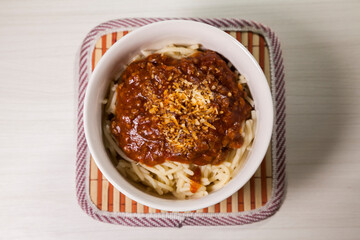 Spaghetti pasta with tomato sauce in white and blue bowl, white wooden background and resting straw plate and cutlery on the side, Brazilian cuisine copy space, top view. Food concept. Pasta concept.