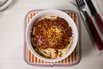 Spaghetti pasta with tomato sauce in white and blue bowl, white wooden background and resting straw plate and cutlery on the side, Brazilian cuisine copy space, top view. Food concept. Pasta concept.