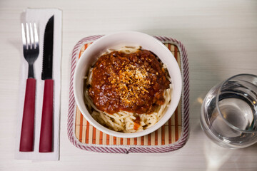 Spaghetti pasta with tomato sauce in white and blue bowl, white wooden background and resting straw plate and cutlery on the side, Brazilian cuisine copy space, top view. Food concept. Pasta concept.