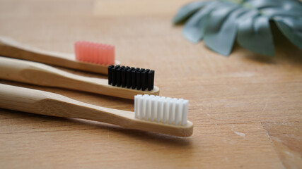 Pink, black and white color of eco-friendly bamboo toothbrushes with blurred leaf on a wood background. Natural organic dental concept