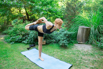 woman doing yoga in the park, young girl doing various wellness exercises, the concept of a healthy...