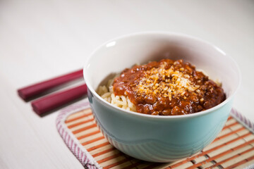 Spaghetti pasta with tomato sauce in white and blue bowl, white wooden background and resting straw plate and cutlery on the side, Brazilian cuisine copy space, top view. Food concept. Pasta concept.