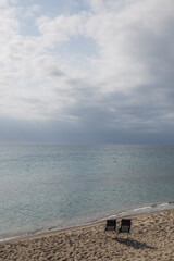 landscape of a beach, there are two chairs on the deserted shore, the sea is calm and the sky cloudy