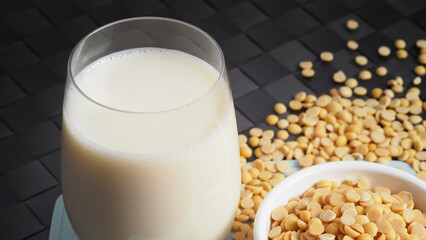 Close-up images of home made healthy drink soy milk with no sugar added in a glass on a green color plastic plate mat and soy beans in small bowl. All of them on black background in a studio shot.