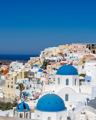 Fototapeta na wymiar Cityscape of Oia town in Santorini island with old whitewashed houses and typical blue domes of orthodox churches, Greece. Greek landscape on a sunny day