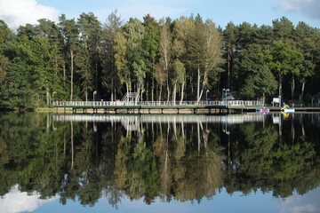 Fototapeta premium Pier and holiday resort on the lake by the forest. Beautiful reflection in the water.