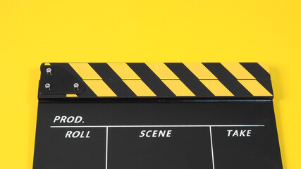 Naklejka premium Clapperboard or movie slate with black&yellow color and film roll on yellow background. It is used in video production and film industry.