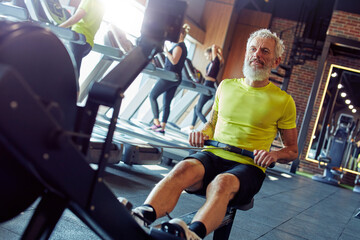 Staying fit and healthy. Strong mature athletic man in sportswear exercising on rowing machine at...