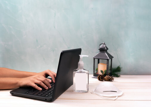 Woman Working On Laptop Computer In Office At Christmas With Face Mask And Hand Sanitizer. 