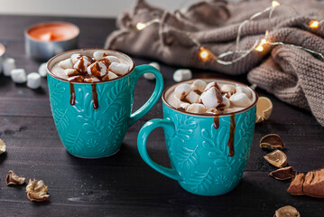 Two turquoise ceramic cups of hot chocolate with marshmallows on a dark wooden table.