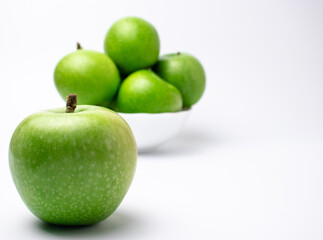 Green apple in front of  white plate with apples.