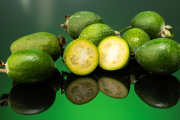 several feijoa fruits scattered on dark glass with gradient background