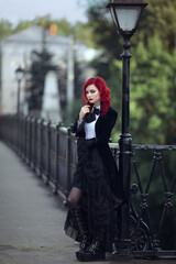red-haired girl stands on the bridge for a year near a black lantern in a black tailcoat